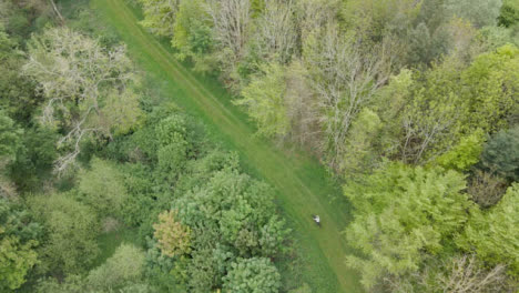 Toma-Aérea-De-Drones-De-Un-Hombre-En-Bicicleta-De-Montaña-Recorriendo-Un-Sendero-A-Través-Del-Campo-Y-El-Bosque-3