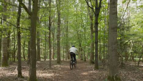 Drone-Tracking-Man-On-Mountain-Bike-Cycling-Along-Trail-Through-Countryside-And-Woodland-