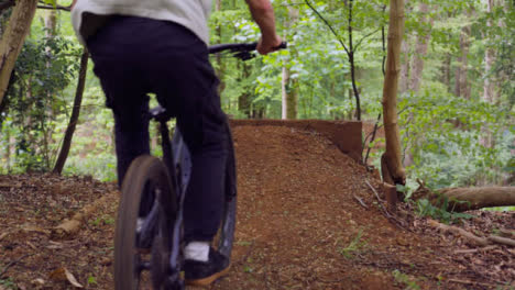 Toma-En-Cámara-Lenta-Del-Hombre-En-Bicicleta-De-Montaña-Haciendo-Saltos-En-El-Aire-En-Un-Camino-De-Tierra-A-Través-Del-Bosque-5