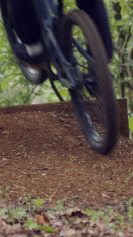 Close-Up-Vertical-Video-Of-Man-On-Mountain-Bike-Making-Mid-Air-Jump-On-Dirt-Trail-Through-Woodland-