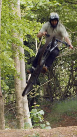 Vertical-Video-Of-Man-On-Mountain-Bike-Making-Mid-Air-Jump-On-Dirt-Trail-Through-Woodland-2