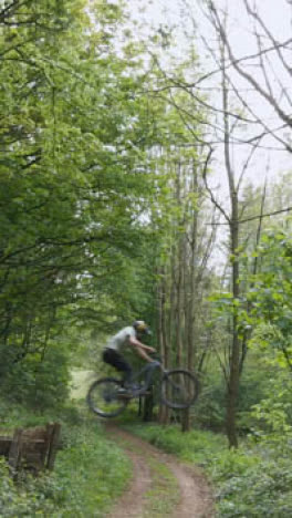 Drone-Vertical-Video-Tracking-Man-On-Mountain-Bike-Cycling-Doing-Mid-Air-Jump-On-Trail-Through-Woodland-2