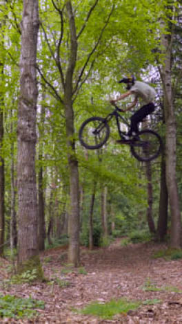 Vertical-Video-Man-On-Mountain-Bike-Making-Mid-Air-Jump-On-Dirt-Trail-Through-Woodland-