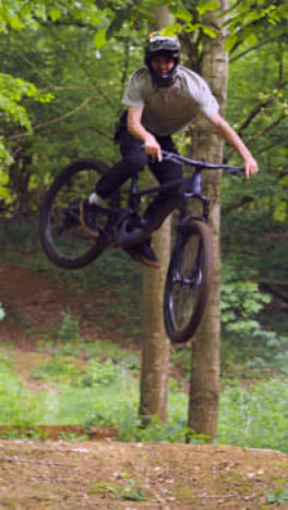 Drone-Vertical-Video-Tracking-Man-On-Mountain-Bike-Cycling-Doing-Mid-Air-Jump-On-Trail-Through-Woodland-4