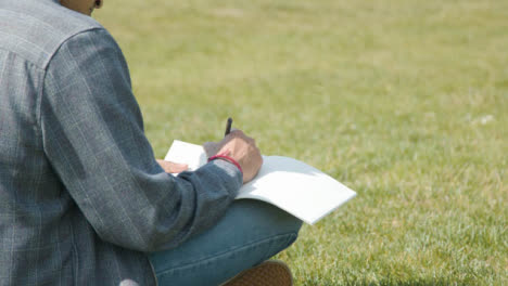 Handheld-Shot-of-a-Student-Writing-Notes-In-a-Park