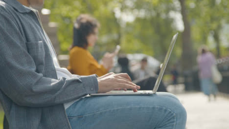 Close-Up-Shot-of-a-Man-Using-Laptop-Sitting-on-Park-Bench