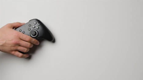 Overhead-Studio-Shot-Of-Hand-Reaching-In-To-Pick-Up-Video-Game-Controller