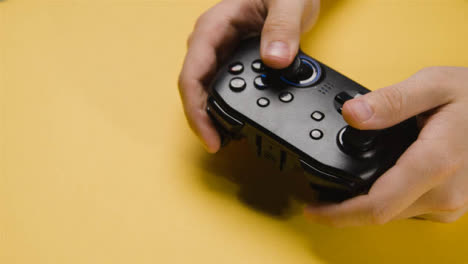 Studio-Close-Up-Shot-Of-Hands-Playing-Video-Game-Controller-Yellow-Background