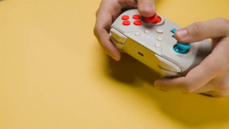 Studio-Close-Up-Hands-Playing-Video-Game-Controller-On-Yellow-Background-1