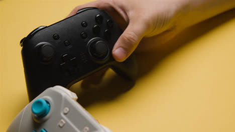 Close-Up-Of-Hand-Picking-Up-One-Of-Two-Video-Game-Controller-Yellow-Background