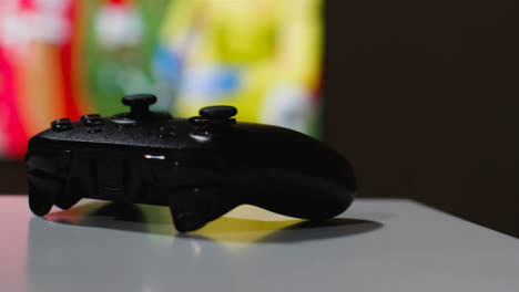 Close-Up-Shot-Of-Video-Game-Controller-With-Game-On-Screen-In-Background