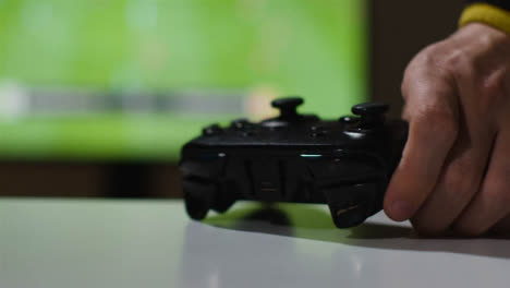 Close-Up-Hand-Picking-Up-Video-Game-Controller-Sports-Game-On-Screen-Background