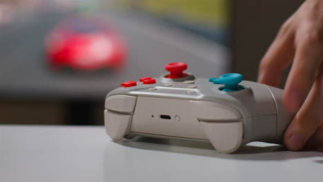 Close-Up-Hand-Picking-Up-Video-Game-Controller-Driving-Game-Screen-Background