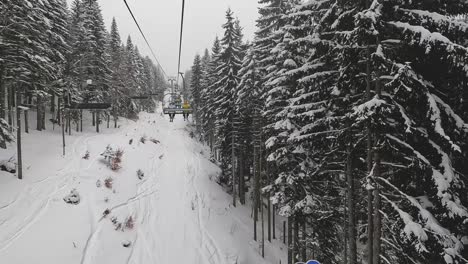 POV-Shot-Of-Skier-On-Chair-Lift-Across-Snow-Covered-Mountain-And-Trees