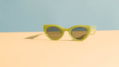 Summer-Concept-Of-Hand-Picking-Up-Sunglasses-On-Yellow-Blue-Background