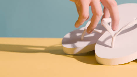 Summer-Concept-Of-Hand-Picking-Up-Flip-Flops-On-Yellow-Blue-Background