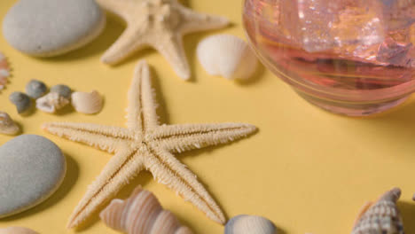 Summer-Holiday-Concept-With-Rotating-Shells-Pebbles-Starfish-Cold-Drink
