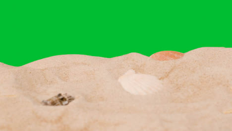 Summer-Holiday-Concept-With-Shells-Starfish-On-Sandy-Beach-In-Foreground-Against-Green-Screen