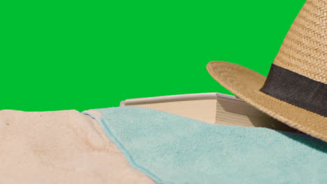Summer-Holiday-Concept-Of-Book-Sun-Hat-Camera-Beach-Towel-On-Sand-Against-Green-Screen