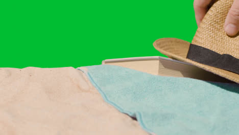 Summer-Holiday-Concept-Of-Book-Sun-Hat-Camera-Beach-Towel-On-Sand-Against-Green-Screen