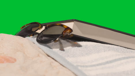 Summer-Holiday-Concept-Of-Book-Camera-Beach-Towel-On-Sand-Against-Green-Screen