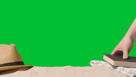 Summer-Holiday-Concept-Of-Book-Sun-Hat-Beach-Towel-On-Sand-Against-Green-Screen