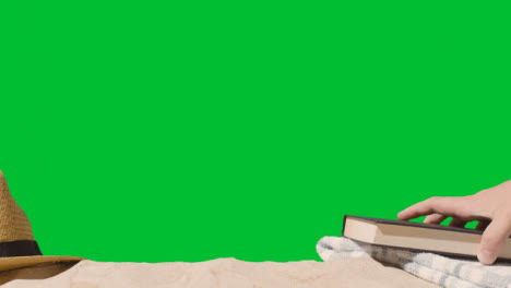 Summer-Holiday-Concept-Of-Book-Sun-Hat-Beach-Towel-On-Sand-Against-Green-Screen-1