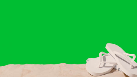 Summer-Holiday-Concept-Of-Flip-Flops-Beach-Towel-On-Sand-Against-Green-Screen