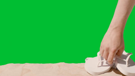 Summer-Holiday-Concept-Of-Hand-Picking-Up-Flip-Flops-Beach-Towel-On-Sand-Against-Green-Screen-1