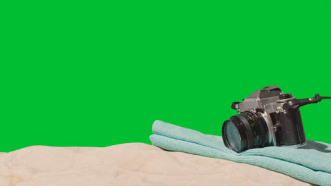 Sommerferienkonzept-Der-Person,-Die-Kamerastrandtuch-Auf-Sand-Gegen-Grünen-Bildschirm-Aufhebt