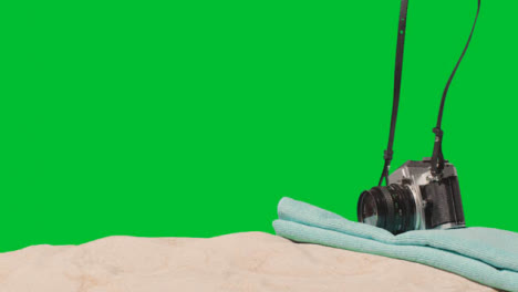 Summer-Holiday-Concept-Of-Person-Putting-Down-Camera-Beach-Towel-On-Sand-Against-Green-Screen