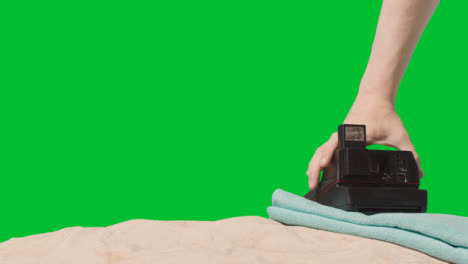 Sommerferienkonzept-Der-Person,-Die-Sofortbildkamera-strandtuch-Auf-Sand-Gegen-Grünen-Bildschirm-Aufhebt