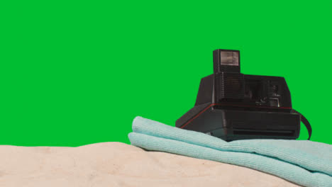 Summer-Holiday-Concept-Of-Person-Putting-Down-Instant-Camera-Beach-Towel-On-Sand-Against-Green-Screen