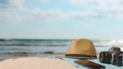 Summer-Holiday-Concept-Of-Camera-Sun-Hat-Mobile-Phone-Beach-Towel-On-Sand-Against-Sea-1