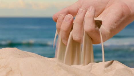 Sommerferienkonzept-Mit-Der-Hand,-Die-Sand-Vom-Strand-Gegen-Meereshintergrund-Aufhebt