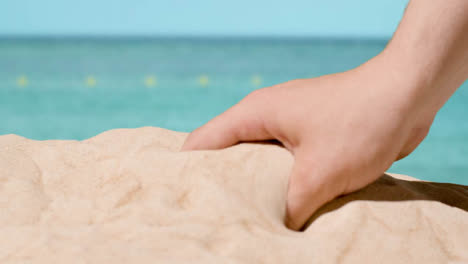 Summer-Holiday-Concept-With-Hand-Picking-Up-Sand-From-Beach-Against-Sea-Background-1