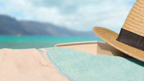 Summer-Holiday-Concept-Of-Book-Sun-Hat-Camera-Beach-Towel-On-Sand-Against-Sea-Background