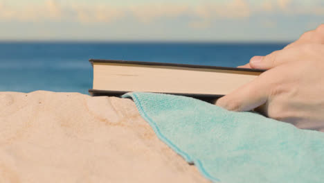 Summer-Holiday-Concept-Of-Person-On-Beach-Towel-Reading-Book-Against-Sea-Background