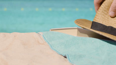 Summer-Holiday-Concept-Of-Book-Sun-Hat-Beach-Towel-On-Sand-Against-Sea-Background