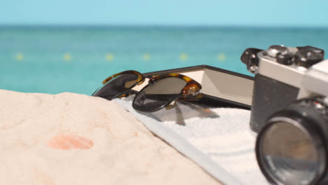 Sommerferienkonzept-Von-Sonnenbrillen-Buchen-Kamera-Strandtuch-Auf-Sand-Vor-Meereshintergrund