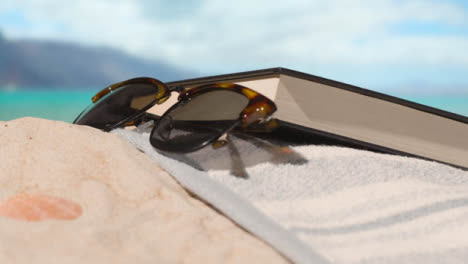 Summer-Holiday-Concept-Of-Sunglasses-Book-Camera-Beach-Towel-On-Sand-Against-Sea-Background
