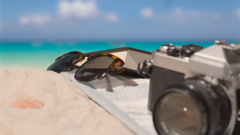 Summer-Holiday-Concept-Of-Sunglasses-Book-Camera-Beach-Towel-On-Sand-Against-Sea-Background-1