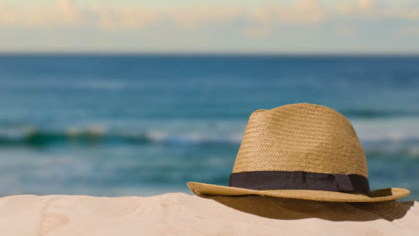 Summer-Holiday-Concept-With-Hand-Picking-Up-Sun-Hat-On-Sand-Against-Sea-Background