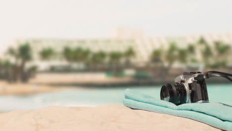 Sommerferienkonzept-Der-Person,-Die-Kamerastrandtuch-Auf-Sand-Gegen-Meer--Und-Hotelhintergrund-Legt