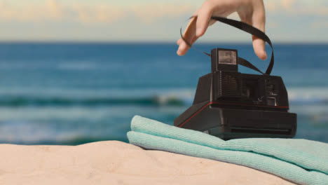 Summer-Holiday-Concept-Of-Person-Putting-Down-Instant-Camera-Beach-Towel-On-Sand-Against-Sea-Background