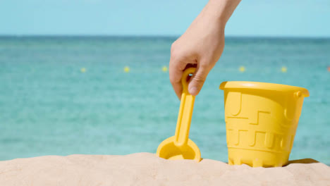 Summer-Holiday-Concept-With-Child's-Bucket-Spade-On-Sandy-Beach-Against-Sea-Background