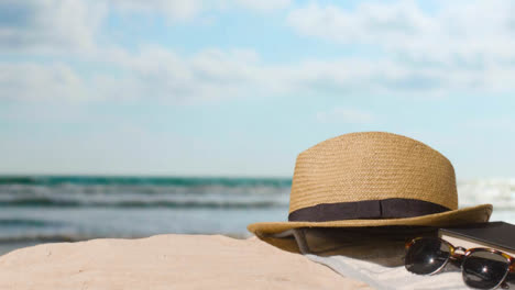 Summer-Holiday-Concept-Of-Sunglasses-Book-Sun-Hat-Beach-Towel-On-Sand-Against-Sea-Background