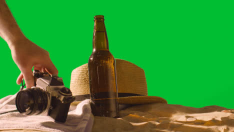 Sommerferienkonzept-Der-Bierflasche-Auf-Strandtuch-Mit-Kamera-Und-Sonnenhut-Gegen-Grünen-Bildschirm-1