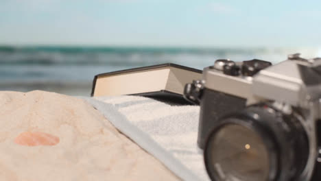 Summer-Holiday-Concept-Of-Book-Camera-Beach-Towel-On-Sand-Against-Sea-Background-1