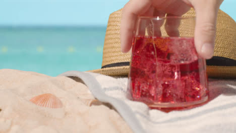 Summer-Holiday-Concept-Of-Cold-Drink-On-Beach-Towel-With-Sun-Hat-Against-Sea-Background